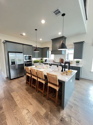 Model Home A modern kitchen with elegant gray cabinetry, hardwood floors, and a central island with woven bar stools.