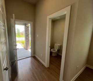 A cozy entryway with wood flooring leads to a half bath, featuring a simple design and natural light streaming in.