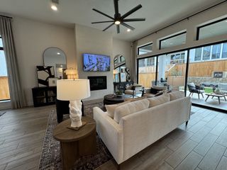 Model Home A modern living room with a cream sofa, large windows, sleek ceiling fan, and stylish decor. The patio outside creates a seamless flow.
