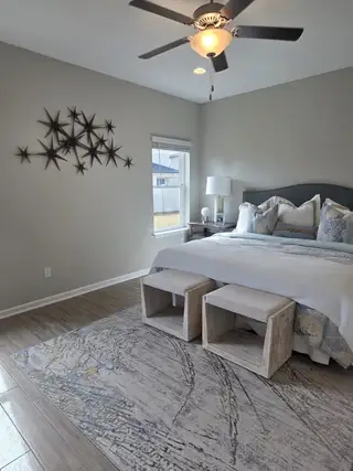 A cozy bedroom featuring a soft rug, stylish wall art, and a ceiling fan, creating a comfortable and inviting atmosphere.