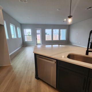 An open-concept space with modern wood floors, ample windows, and a sleek kitchen island featuring a stainless dishwasher.