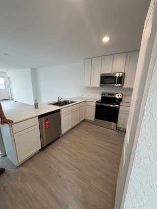 Model Home A modern kitchen with white cabinetry, stainless steel appliances, and wood-style flooring in a spacious open-concept layout.