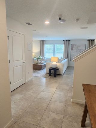 Model Home A bright hallway with tiled floors leading to a cozy living area, featuring a plush white sofa and soft natural lighting.