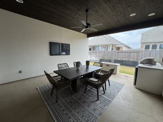 A covered outdoor dining space with a built-in TV, ceiling fan, and grill station in Veramendi by Scott Felder Homes (New Braunfels, TX).