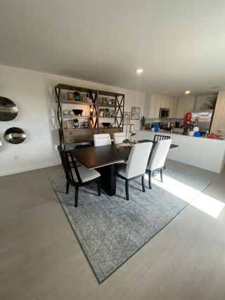 Model Home A modern dining area with a sleek table, elegant chairs, and a decorative shelf, adjacent to a bright kitchen space.