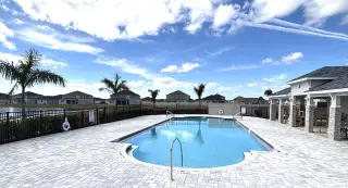 A community pool with palm trees and seating in the Gardens at Waterstone II by KB Home (Palm Bay, FL).