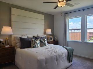 A cozy bedroom with a modern upholstered headboard, elegant lamps, and a ceiling fan, filled with natural light.
