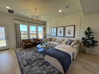 A cozy living room with a large sectional, elegant chandelier, and natural light from tall windows, complemented by modern decor.