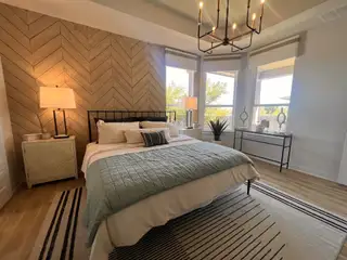 Model Home A cozy bedroom featuring a herringbone accent wall, stylish lighting, and large windows with elegant decor.