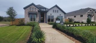 A charming brick and siding home with elegant dark trim and lush landscaping in Kallison Ranch by Perry Homes (San Antonio, TX).