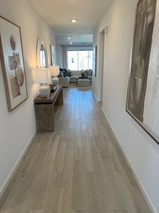 A welcoming hallway with wood-style floors, abstract artwork, and elegant lighting leading to a cozy living space.