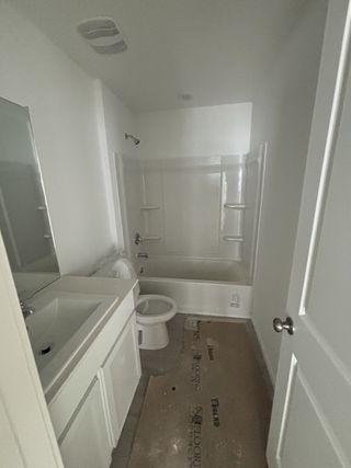 A modern bathroom with a sleek white vanity, built-in bathtub, and neutral tile flooring.