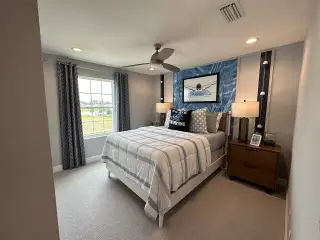 A cozy bedroom featuring a stylish bed, nautical-themed decor, and ample natural light through a large window.