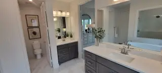 A luxurious primary bathroom with dual vanities, framed mirrors, and elegant dark cabinetry, exuding a modern yet timeless appeal.
