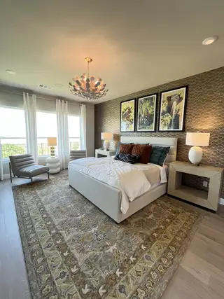 A chic bedroom featuring a plush bed, artistic wallpaper, elegant chandelier, and cozy seating by the window.