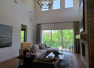 A spacious living room with high ceilings, large windows, cozy seating, and a chic chandelier.