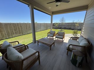A cozy patio with elegant wicker furniture, overlooking a lush green lawn and fenced backyard, perfect for relaxation.