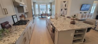 Model Home A spacious kitchen with granite countertops, gray cabinets, and a center island, flowing into a dining area, in a Stillwater Ranch home by Coventry Homes (San Antonio, TX).