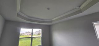 A room with a tray ceiling, recessed lighting, and a window overlooking a grassy yard.