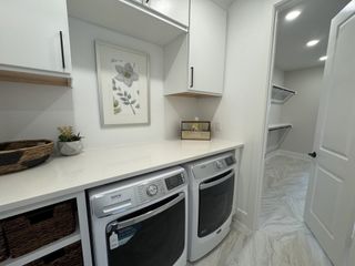 A sleek laundry room featuring modern appliances, white cabinetry, and elegant tile flooring.