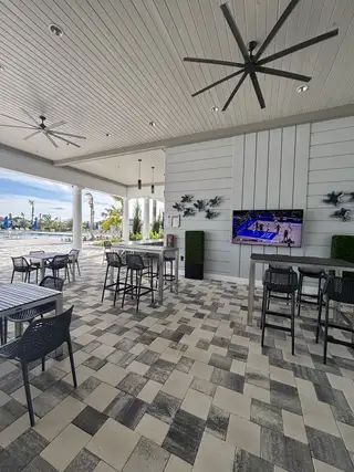 Stylish outdoor lounge with patterned tile, modern seating, large fans, and a wall-mounted TV, perfect for relaxation.
