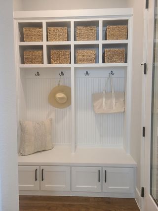 A chic mudroom with white cabinetry, wicker baskets, hooks, and seating, offering stylish storage and organization.