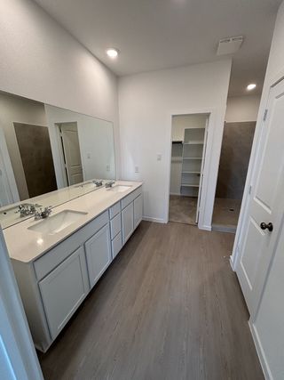 A sleek bathroom with dual sinks, spacious countertop, light wood flooring, and a large mirror.
