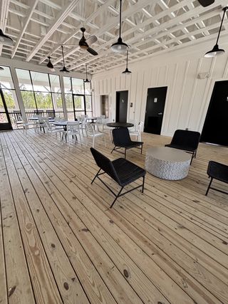 An airy outdoor patio with wooden flooring, modern black wicker chairs, and ceiling fans for a relaxed vibe.