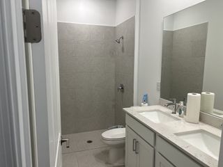 A modern bathroom with dual sinks, a large mirror, and sleek gray tiles in the shower.