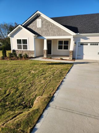 A charming light-gray home with stone accents and a fresh lawn in Grove At Gin Branch by Mattamy Homes (Wendell, NC).