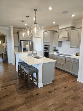 A contemporary kitchen with sleek gray cabinetry, pendant lights, and a central island with bar stools on hardwood floors.
