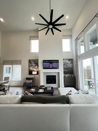 A spacious living room with a tall ceiling, large modern fan, cozy fireplace, and expansive windows for natural light.