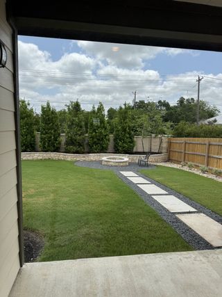 A welcoming backyard patio with manicured lawn, stone fire pit, and paved path under a bright sky.