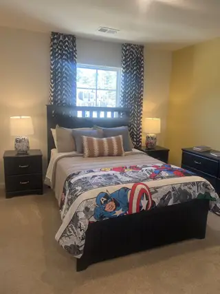 A cozy bedroom featuring a bold superhero-themed bedspread, dark furniture, and patterned curtains.