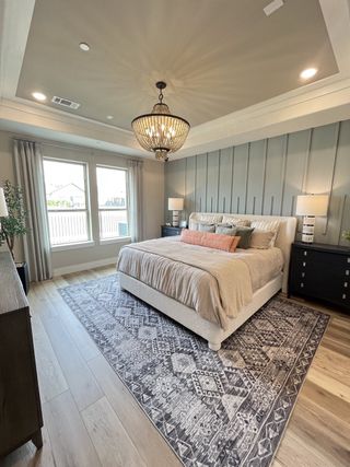 Model Home A cozy bedroom with a stylish chandelier, patterned rug, and large windows offering natural light.
