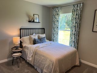 Model Home A cozy bedroom with a metal bed frame, layered bedding, and floral curtains framing a sunny window.