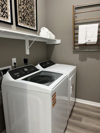 A modern laundry room with sleek appliances, wooden drying rack, artistic wall decor, and light wood flooring.
