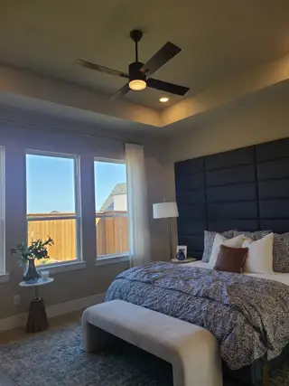 Model Home A cozy bedroom with a plush bed, modern ceiling fan, and large windows bringing in natural light.
