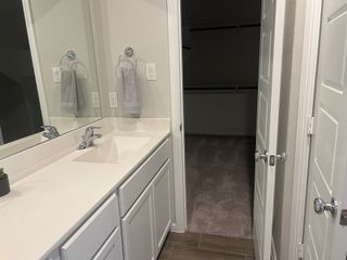A modern bathroom with dual sinks, marble-tiled shower walls, and sleek white cabinetry in Woodmere by M/I Homes (Denton, TX).