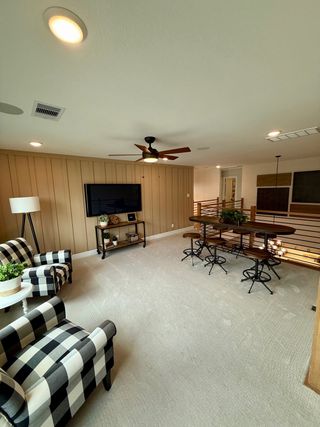 Model Home A cozy lounge with plaid chairs, a TV, and a high-top table set under warm lighting and a ceiling fan.