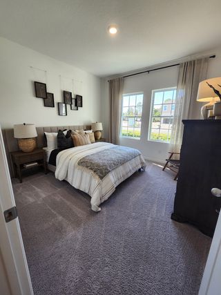 A cozy bedroom with plush carpeting, modern decor, and ample natural light through large windows.