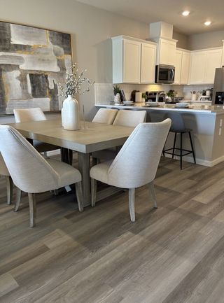 A modern dining area with elegant beige chairs, a sleek table, and an open kitchen showcasing white cabinets and stylish decor.