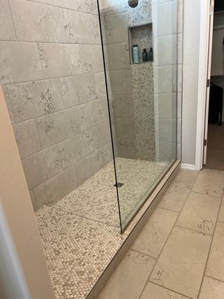 A sleek bathroom with a glass-enclosed shower, featuring pebble mosaic tiles and elegant wall detailing.