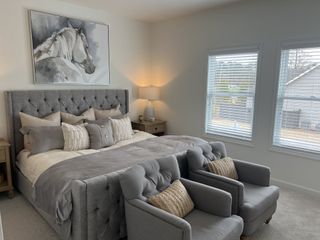 Cozy bedroom with a plush, tufted gray headboard, elegant decor, and soft natural light from large windows.