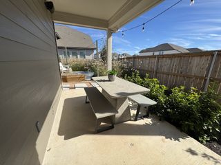 A cozy patio with a modern concrete table, benches, string lights, and privacy fence. Perfect for relaxing outdoors.