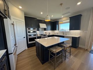 A modern kitchen with navy cabinets, a large island, pendant lights, and stainless steel appliances.
