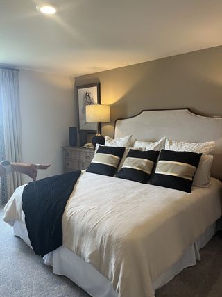 A cozy bedroom with a plush, beige headboard, elegant bedding, and soft lighting on a wooden side table.