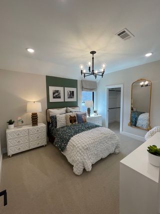 A cozy bedroom with elegant décor, featuring a plush bed, modern chandelier, and gold-framed mirror.