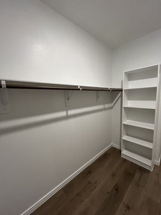 A spacious walk-in closet with sleek shelving and dark wood floors, offering ample storage and organization space.