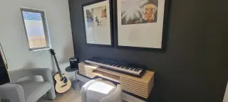 A modern music nook with a keyboard, guitar, and chic art prints on a dark accent wall. Perfect for creative inspiration.